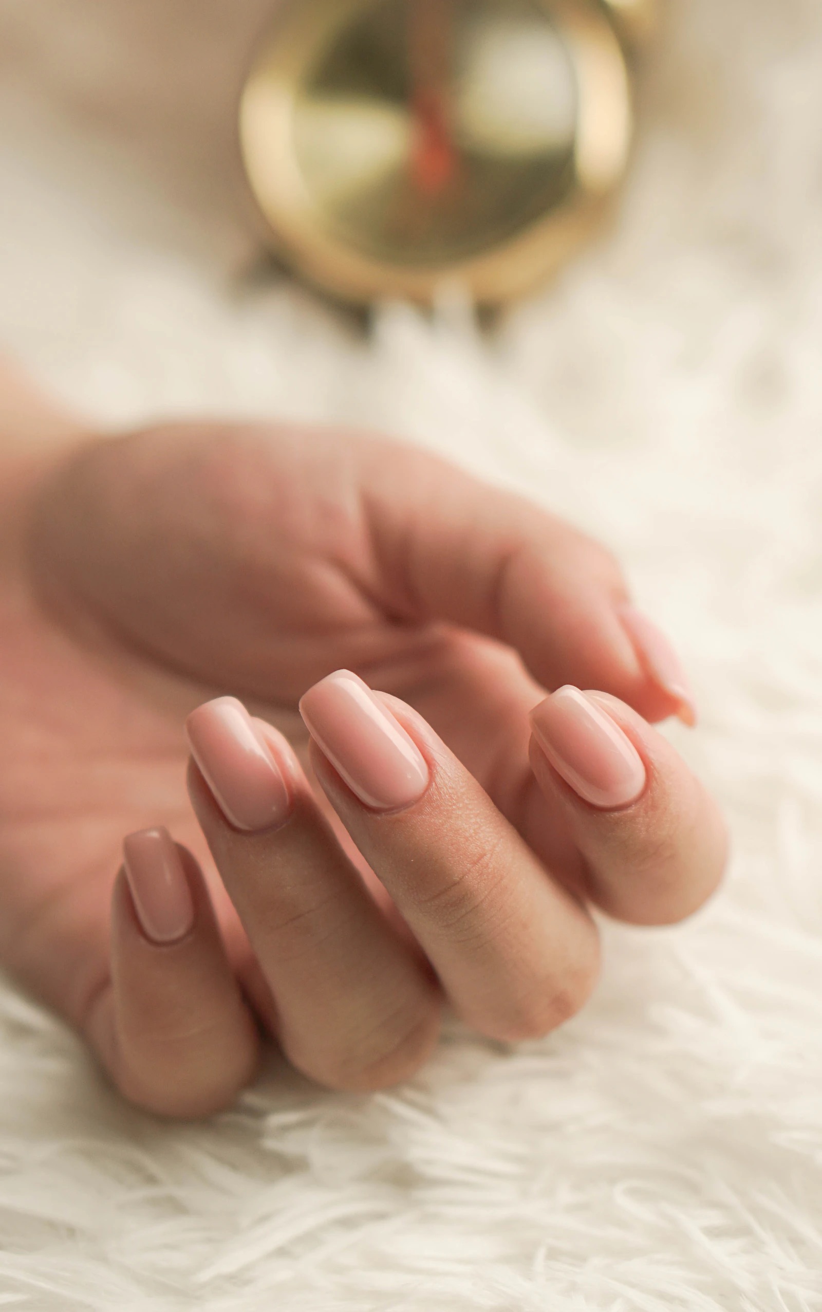 A hand with light pink manicured nails resting on a white surface